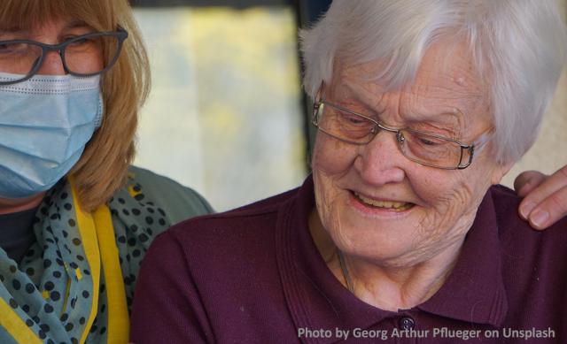 Woman wearing protective face mask helps older woman