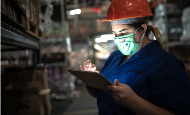 Latina wearing hard hat and COVID mask looking at clipboard