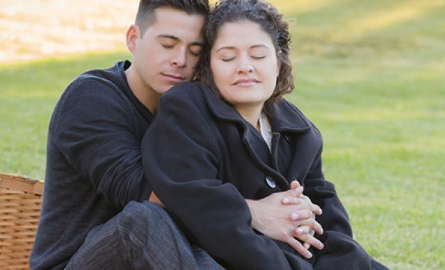 Latinx couple with man cuddling pregnant woman in a park