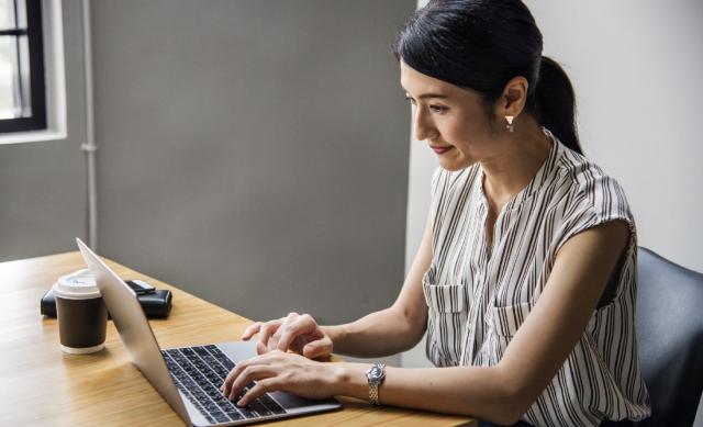 Woman with her hair in a ponytail wearing business attire sitting at desk working on a laptop computer