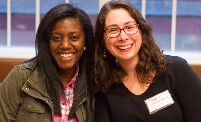 Two young women sitting next two each other facing foward and smiling.
