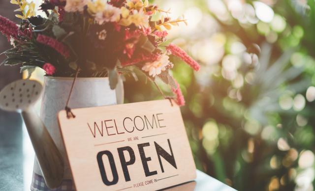 Welcome - open sign leaned up against bouquet of flowers in a watering can