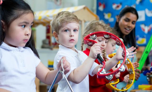Four children in daycare playing with musical instruments with daycare worker in background