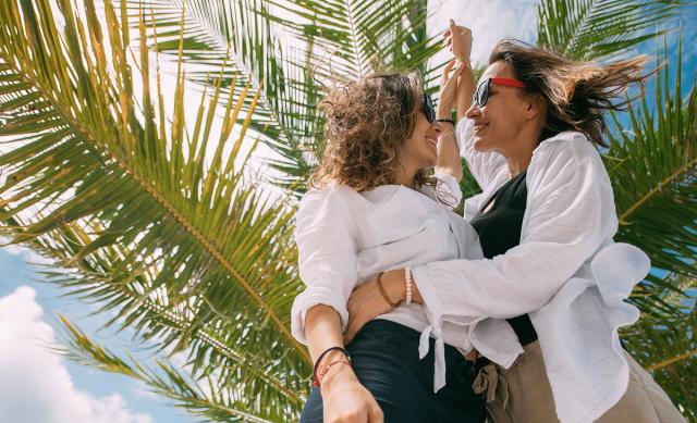 Lesbian couple smiling and embracing with tropical plant in background