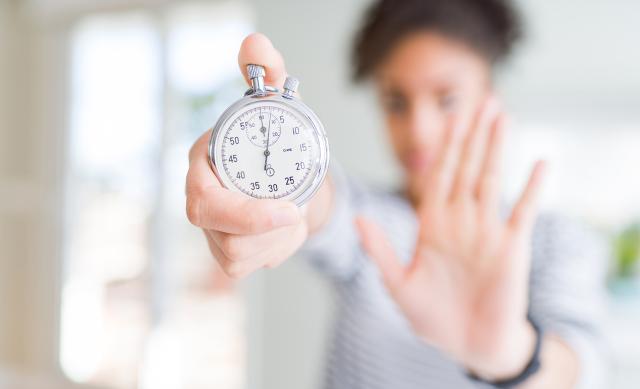 Woman holding stopwatch in right hand and holding her left hand up in a "stop" gesture