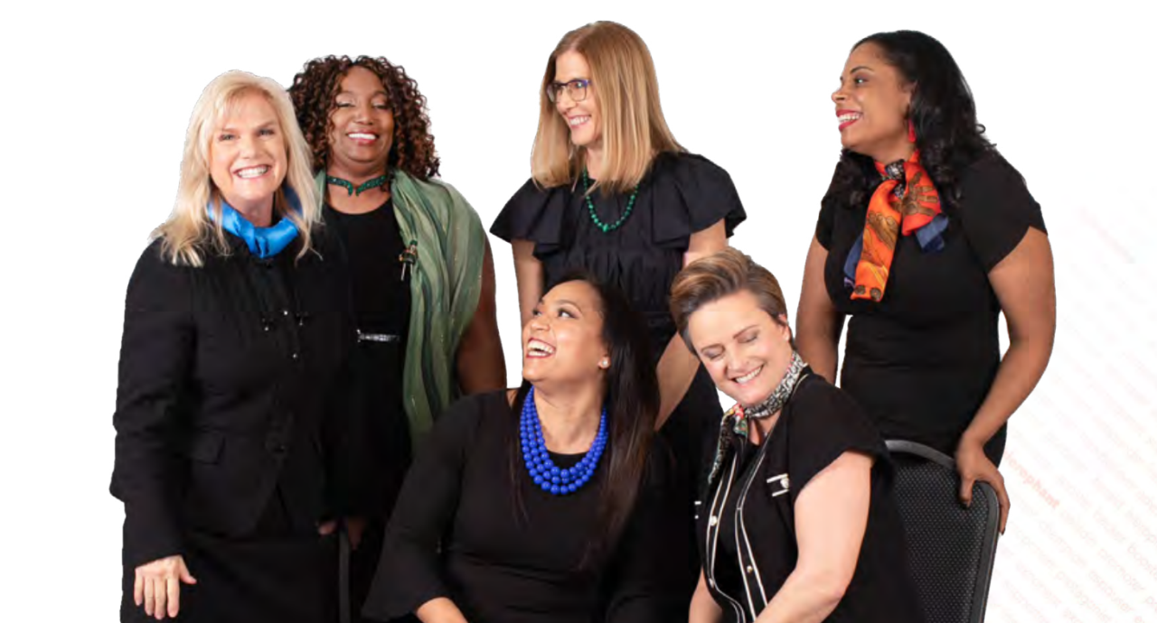 Six diverse women wearing professional clothing in a group smiling and laughing