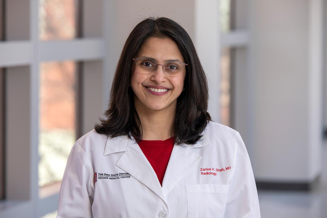 A woman smiles in a white coat.