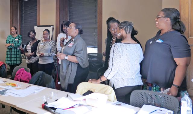 Black women standing behind a table in a meeting room, some having a conversation
