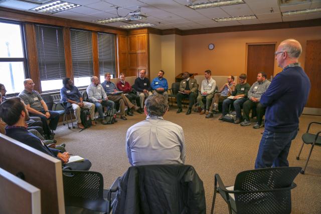 one man speaks in front of a room of men.