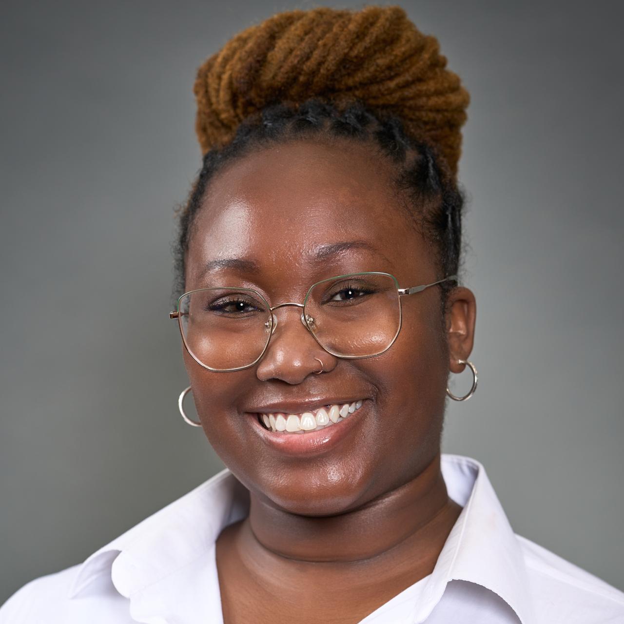 Kylee Smith smiling and wearing a white shirt in front of a dark gray wall.