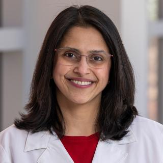 A woman smiles in a white coat.