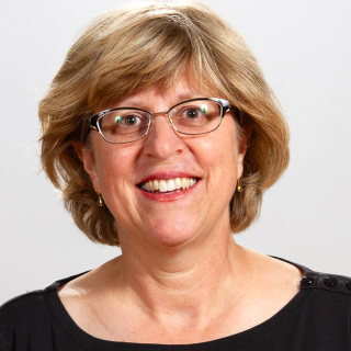 Portrait of Athena Yiamouyiannis wearing a black scoop neck blouse in front of a gray background