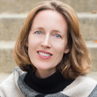 Jen Shanahan wearing a black and beige patterned sweater sitting in front of concrete stairs.