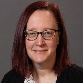 Melissa Buelow standing in front of a dark gray background.