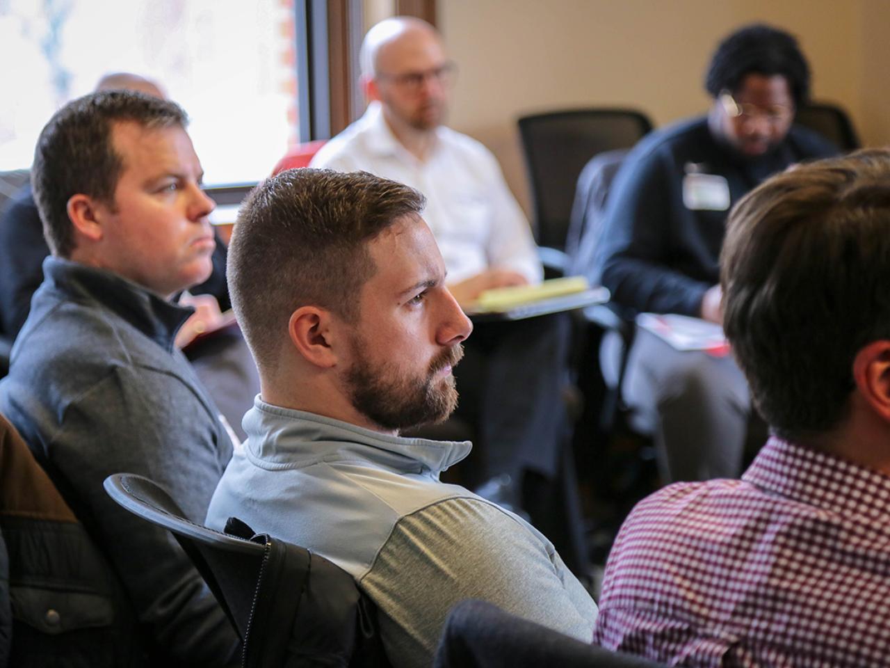 Five men sitting in a larger circle listening to workshop presenter