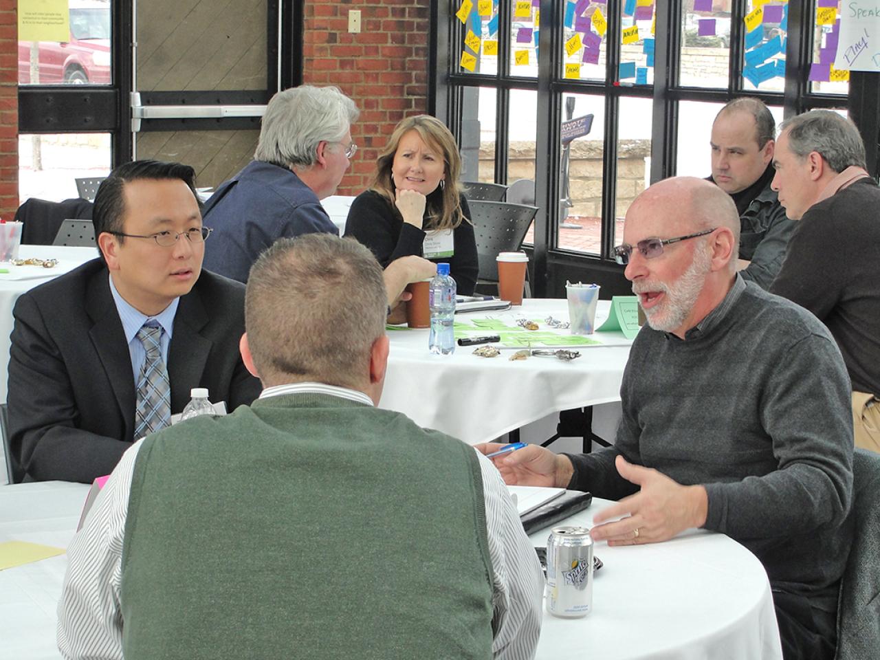 Two groups of people in business casual clothing sitting around round tables having conversations.
