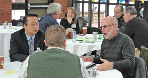 Two groups of people in business casual clothing sitting around round tables having conversations.