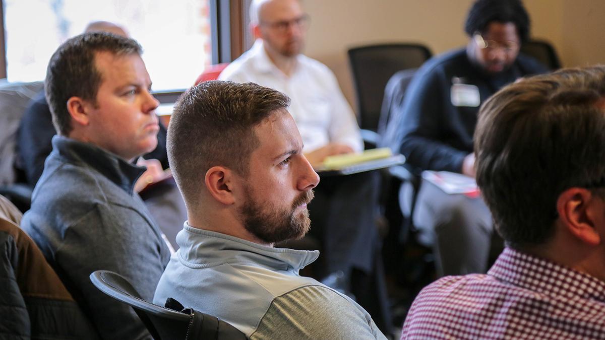 Five men sitting in a larger circle listening to workshop presenter