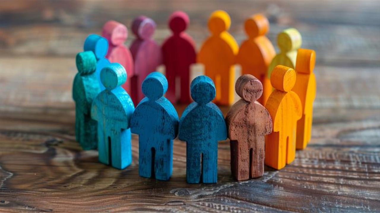 A group of colorful wooden figures that look like people positioned in a circle on a wooden table. 